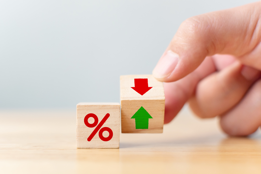 Hand adjusting wooden blocks with a red percentage sign and arrows indicating up and down, symbolising changes in interest rates.