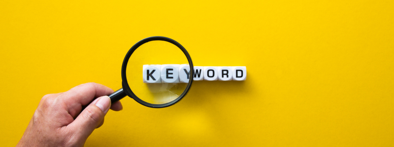 Magnifying glass focusing on blocks spelling the word 'KEYWORD' on a bright yellow background, symbolising keyword research or SEO focus.