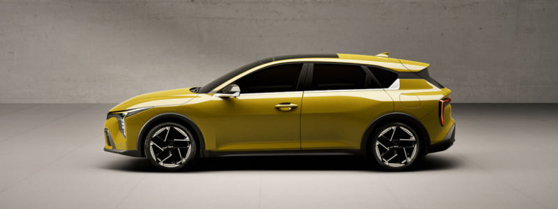 The yellow Kia K4 parked side on against a grey concrete background.