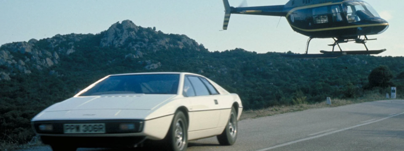 The classic Lotus Esprit driving on a road with a helicopter floating in the background, taken from a Bond film.