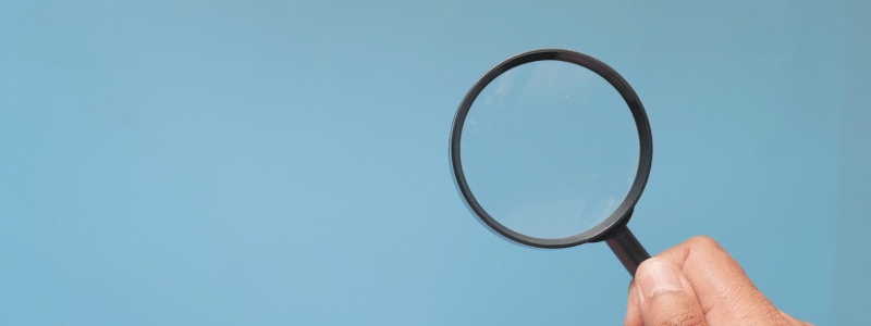 A hand holds a magnifying glass up, against a light blue background.