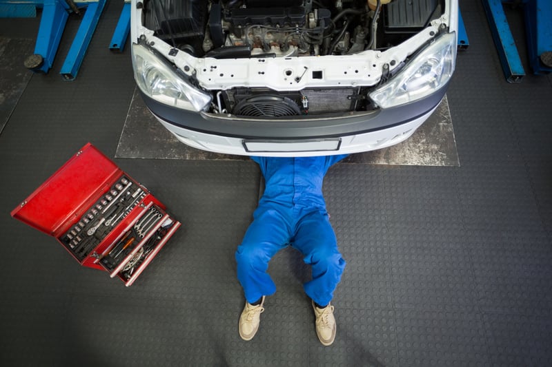 Mechanic lying and working under car at the repair garage.