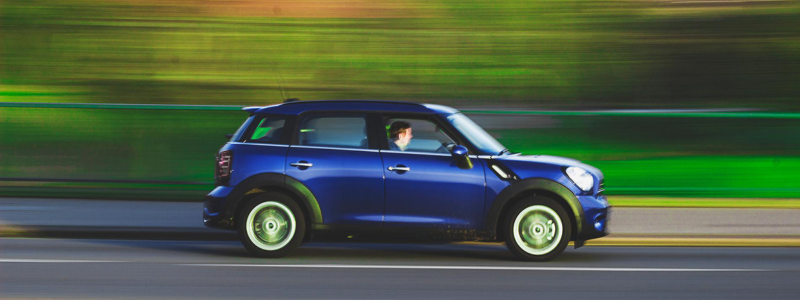 A blur of a blue Mini driving on a road, showing it driving at speed.