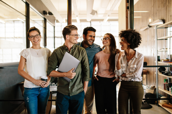 
A group of diverse young professionals stand in a modern office, smiling and chatting.