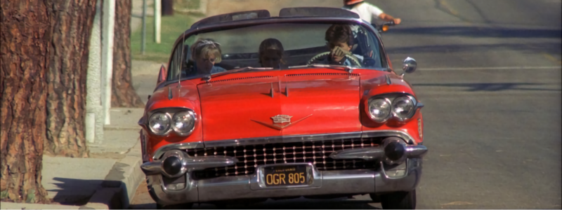 A the red Cadillac in Nightmare On Elm Street, driving down a sunlit road.