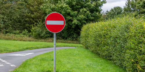 A red no entry sign stood up in a rural setting, blocking people from using a particular part of road.