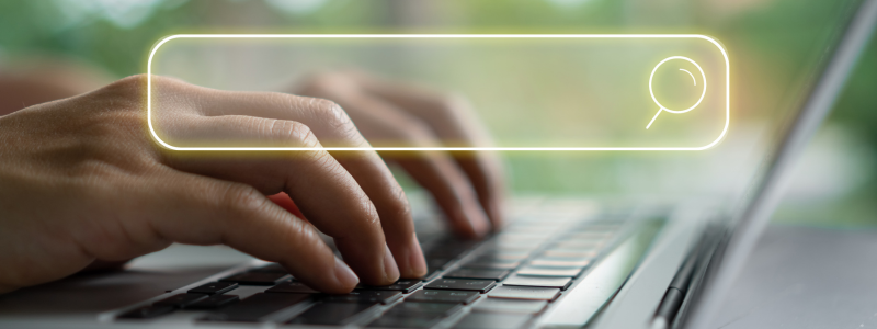 Hands typing on a laptop keyboard with an illuminated search bar icon, symbolising online searching, browsing, or digital research.