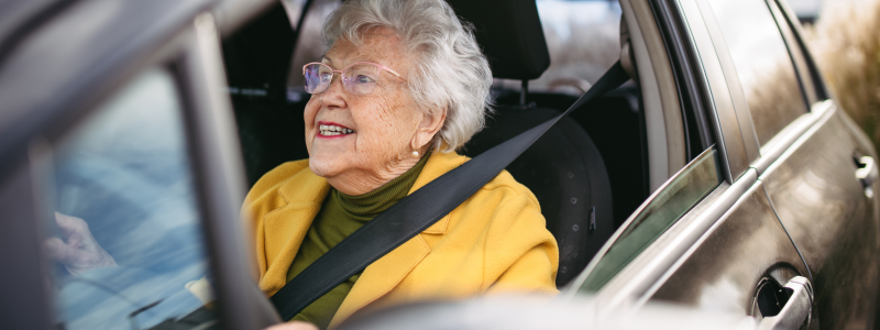 An old woman driving her car whilst smiling.