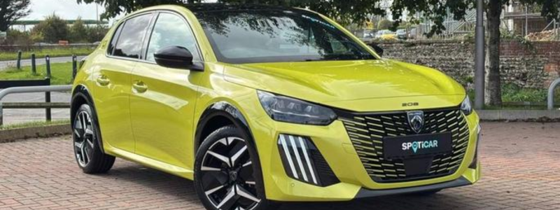 A yellow Peugeot 208 parked up in a parking area in a day time setting. 