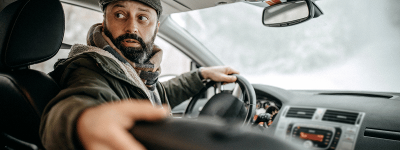 A driver looks backwards whilst resting their hand on the top of the passenger seat, likely in an attempt to see behind whilst reversing.