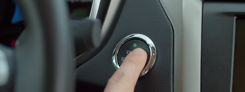 A finger pressing on an engine start button in a car.