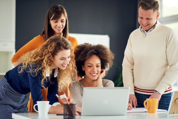 A group of diverse coworkers engaging enthusiastically over a project on a laptop, sharing ideas in a vibrant office environment. The setting is casual, promoting teamwork and creativity.