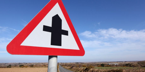 A t-junction sign stood up with a rural background and road passing through.