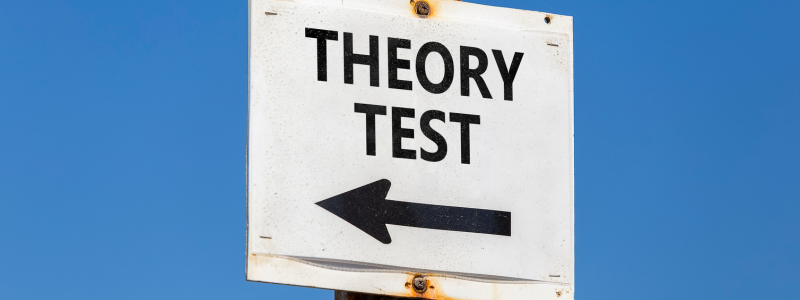 A white sign with 'THEORY TEST' written on and an arrow pointing in the direction of where the tests are. 