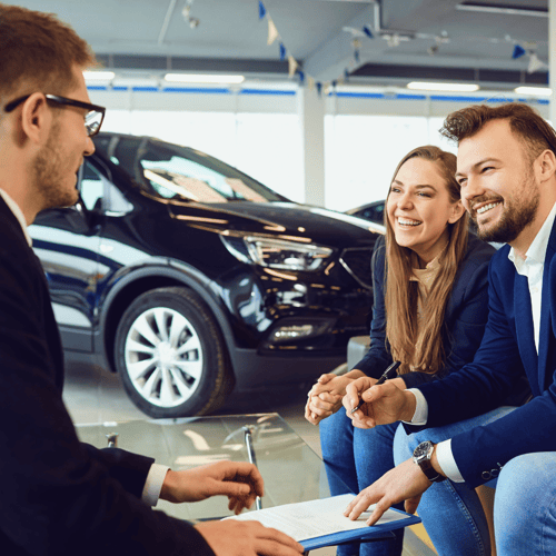 A couple signing a contract for a vehicle in a car dealership.