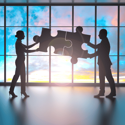 Two business people join large jigsaw pieces against a bright background.