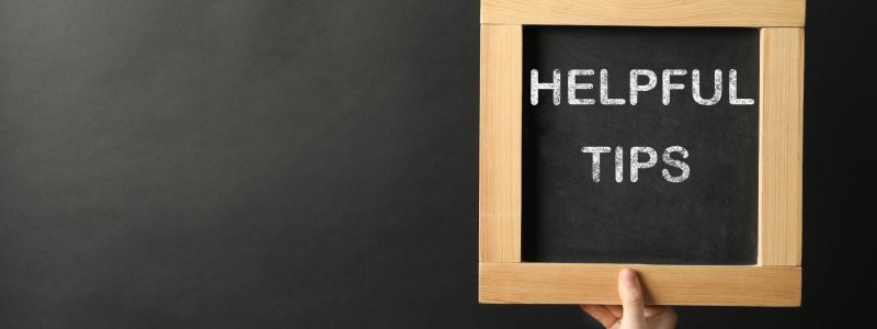 A hand holds up a frame with 'HELPFUL TIPS' written behind it, against a black chalkboard.