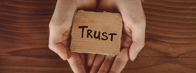 Hands gently holding a piece of cardboard with the word 'Trust' written on it, symbolising care, reliability, and the importance of building trust.