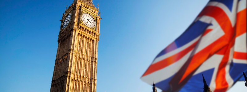 An upward view of Big Ben, with a British flag in focus in the corner.