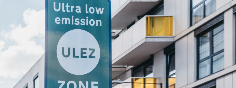 A blue ULEZ zone sign with a block of residential flats in the background.