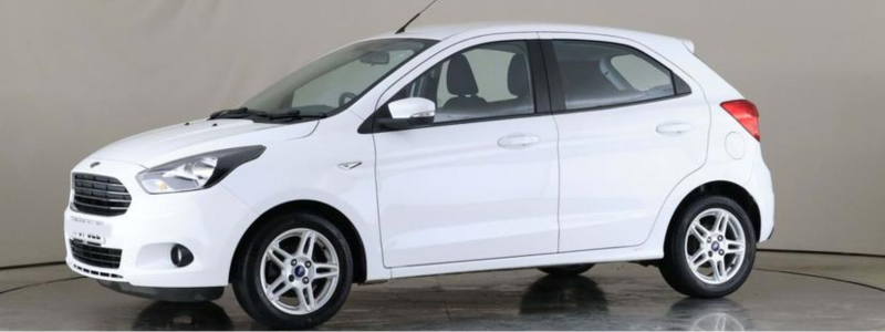 A side-on view of a white Ford Ka Plus, parked against a grey backdrop, likely in a car showroom.