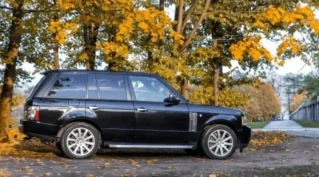 A black Range Rover parked side-on against a group of trees, all with yellow leaves on them.